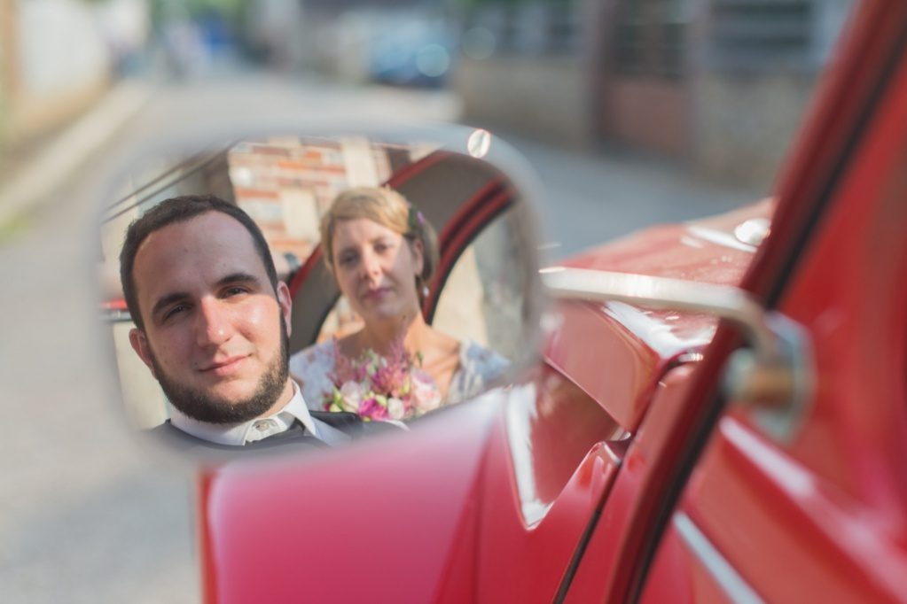 Reflet des mariés dans le rétroviseur d'une voiture rouge – vidéaste et photographe mariage
