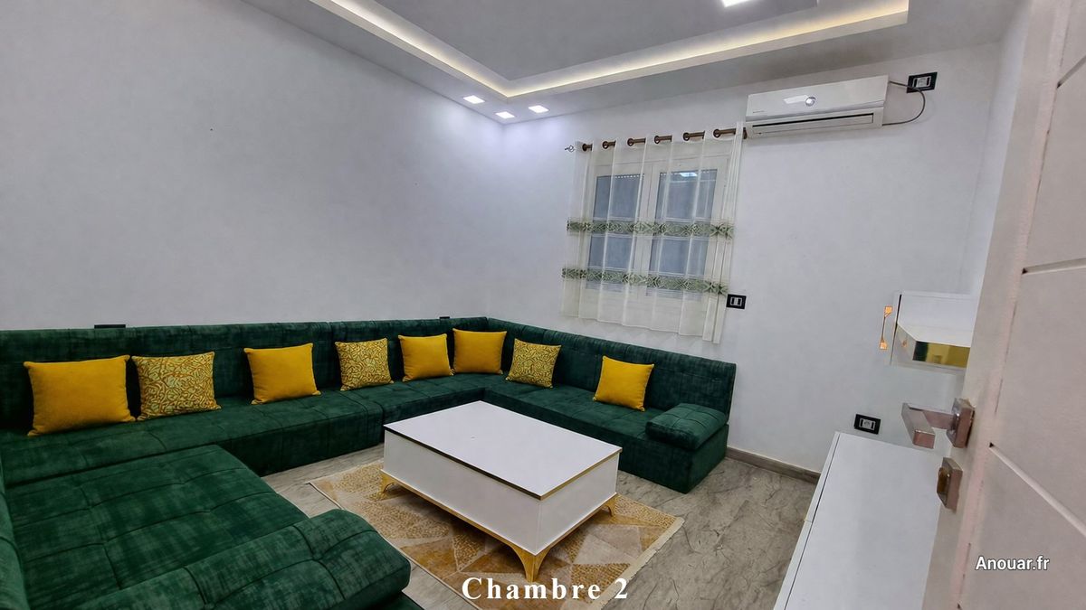 Chambre 2 aménagée avec grand canapé d’angle vert et climatisation